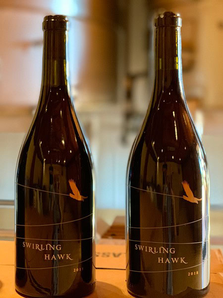Two wine bottles labeled Swirling Hawk with a bird logo, placed on a wooden surface.